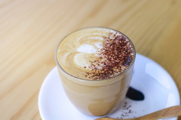 Hot latte juice in a glass with a white coaster with a wooden spoon placed on a beautiful wood table.