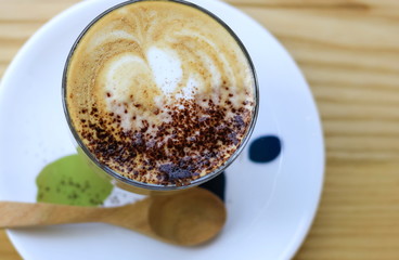 Hot latte juice in a glass with a white coaster with a wooden spoon placed on a beautiful wood table.