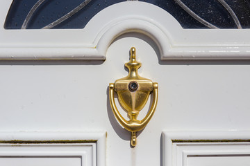 Golden door knocker with peephole on a white door