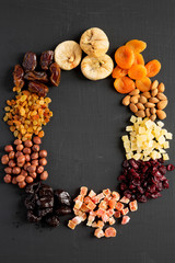 Frame of dried fruits and nuts on black surface, top view.