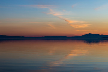 Symmetrcal, beautiful view of Trasimeno lake (Umbria, Italy) at sunset, with orange and blue tones in the sky