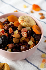 Dried fruits and nut mix in a pink bowl on cloth, side view. Close-up.