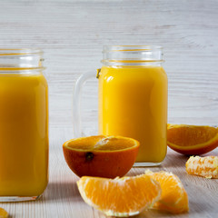 Homemade fresh orange juice in glass jars over white wooden background, side view. Close-up.