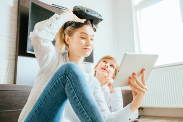Mother with virtual reality headset and son sitting on floor using digital tablet. Happy mom and little boy using tablet with touchscreen watching a video. Smiling sister and brother playing on tablet
