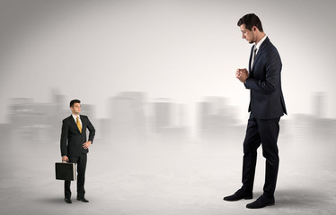 Obraz premium Gigantyczny biznesmen boi się małego poważnego wykonawcy z walizką