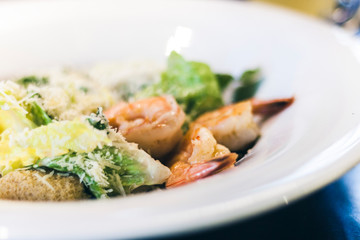 Caesar salad with shrimps on white plate in restaurant.