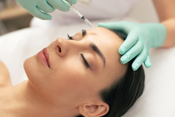 Naklejka premium Face of calm woman and hand making injection into forehead