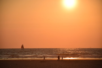 Naklejka na ściany i meble Walking on a Dutch beach with the setting sun with a sailboat in the distance