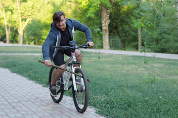 Young caucasian man bicycling in the green park put the spoke in a wheel. Concept of stupid act...