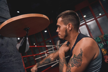 New champion. Close-up of muscular tattooed boxer in sports clothing hitting punching speed bag while training his boxing skills in boxing gym