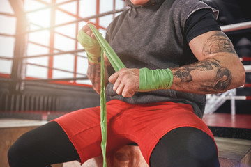 He is a new champion. Strong tattooed athlete in sports clothing wrapping hands with green boxing wraps, close-up of strong hands and fist ready for fight - Powered by Adobe