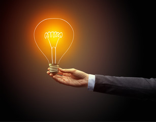 Hand holding light bulb on dark background, new idea concept