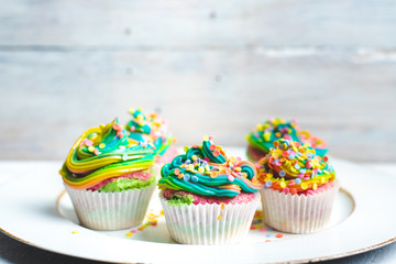 beautiful, bright, very colorful muffins decorated with rainbow cream and candy confetti, on a bright, spring background