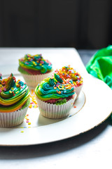 beautiful, bright, very colorful muffins decorated with rainbow cream and candy confetti on a white, wooden plate