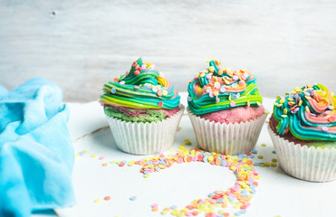 beautiful, bright, very colorful muffins decorated with rainbow cream and candy confetti, on a bright, spring background