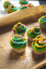 beautiful, bright, very colorful muffins decorated with rainbow cream and candy confetti, on a bright, spring background