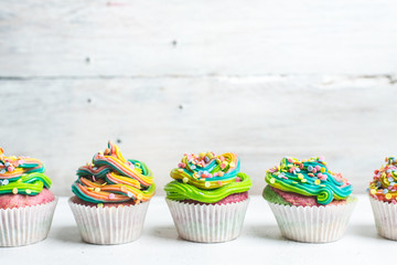 beautiful, bright, very colorful muffins decorated with rainbow cream and candy confetti, on a bright, spring background