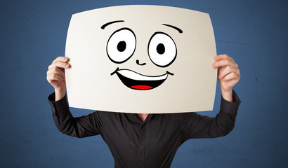 Young student holding a paper with laughing emoticon in front of his face

