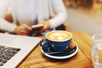 Close up of espresso on desk. In background woman using smart phone.