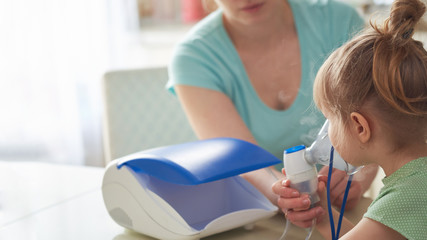 a woman makes inhalation to a child at home. brings the nebulizer mask to his face. inhales the...