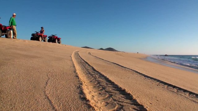 Group of tourists on quad bike ATV ride on sandy shore. Quad-riders ride on sandy hills. Concept of outdoor activities and travel.