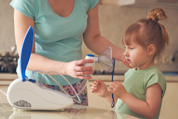 a woman makes inhalation to a child at home. brings the nebulizer mask to his face. inhales the...