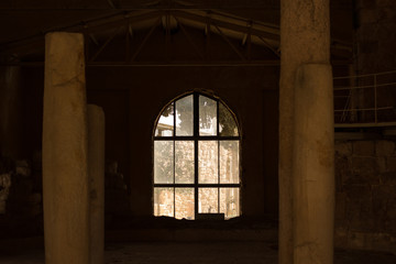Fototapeta na wymiar abandoned partly destroyed stone poor building interior inside environment symmetry foreshortening with columns and arch shape window in the center