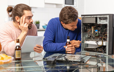 Two men repairing a desktop computer and drink beer