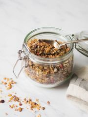 Nuts, seeds, goji berries granola in open glass jar. Healthy breakfast - homemade granola in a jar on a marble white background