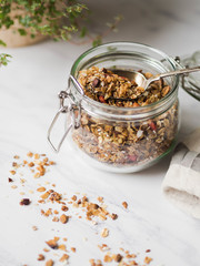 Nuts, seeds, goji berries granola in open glass jar. Healthy breakfast - homemade granola in a jar on a marble white background