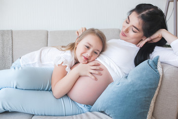 Obraz na płótnie Canvas Pregnant woman and her little daughter having fun indoors. Maternity. Young mother waiting for a baby birth with little cute daughter. Family together.