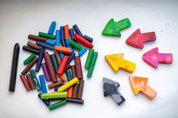 made homemade wax pencils from the wreckage of old crayons by melting them in the oven at high temperature in silicone form. crayons in the form of arrows lie on paper, hand child