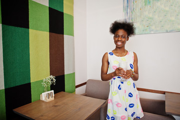 Сheerful african american young woman in summer dress at cafe drinking milkshake.