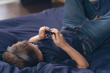 boy listening to music in headphones while lying in bed selective focus on head