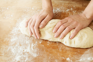 woman's hands and dough yeast  lying on a wooden cutting board sprinkled with flour