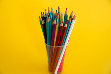 Colored wooden pencils for drawing in a glass stand on a yellow background. Children's multi-colored pencils for drawing.