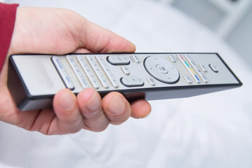 man's hand using the tv remote control from the bed