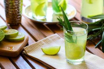 Natural homemade lemonade with lemon rosemary and mint in glasses on wooden table at the terrace. Cold refreshing beverage for hot summer day.