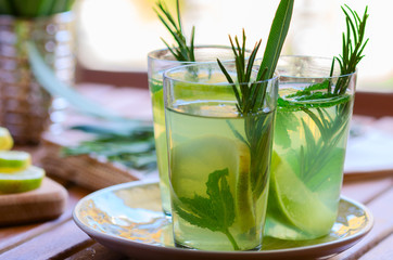 Three glasses with atural  lemonade made from  lemon rosemary and mint in glasses on wooden table at the terrace. Cold refreshing beverage for hot summer day.