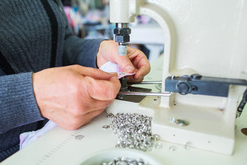 Closeup view of hands of sewer attaching metal round snaps to baby clothes with help of special machine at garment factory. Horizontal color photography.