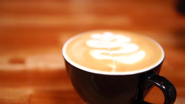 Close up slow motion view on beautiful flower coffee latte art made with hot milk foam in black cappuccino cup