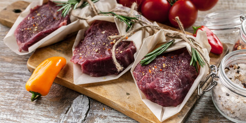 Raw meat steaks, rosemary, sweet peppers and cherry tomatoes. Fresh meat on a cutting board, herbs and vegetables