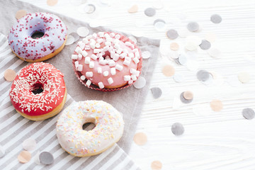 Delicious colorful donuts with sprinkles and marshmallows on stylish white table with confetti, copy space. Party concept. No diet. Candy bar at wedding reception. Purple, pink donuts