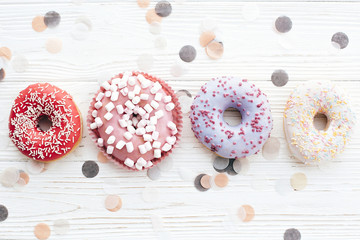 Delicious colorful donuts with sprinkles and marshmallows on stylish white table with confetti,...