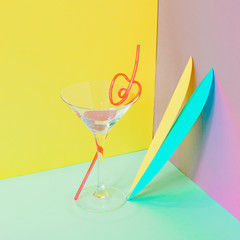Cocktail glass with funny drinking straw and colorful tropical leaves. Strong fashion shadows. Concept of luxury relax with beverage on the beach.