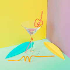 Cocktail glass with funny drinking straws and colorful tropical leaves. Strong fashion shadows. Concept of luxury relax with beverage on the beach. Minimalism