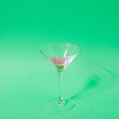 Cocktail glass with funny pink liquid on green background. Strong fashion shadows. Concept of luxury relax with beverage on the beach.