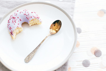 Delicious bite of donut with sprinkles on stylish plate with spoon on white table with confetti. Party concept. No diet. Candy bar at wedding reception. Purple donut