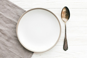 Stylish empty plate with vintage spoon on napkin on white table, flat lay. Modern set, serving for reception and celebration. Party and diet concept. Copy space