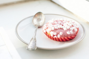 Delicious colorful donut with sprinkles and marshmallows on stylish plate on white table with spoon. Party concept. No diet. Candy bar at wedding reception. Pink donut
